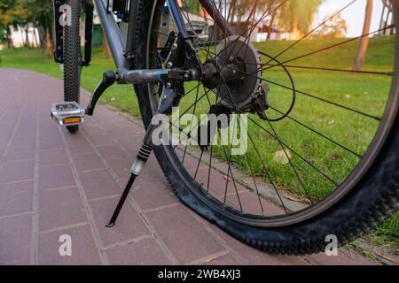 Fahrrad mit flachem Hinterrad in einem Stadtpark aus nächster Nähe. Reparatur von Fahrradrädern Stockfoto