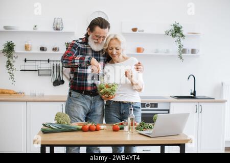 Das alte kaukasische Paar verbringt Zeit zur freien Verfügung, um in der modernen hellen Küche Frühstück zu kochen. Stockfoto