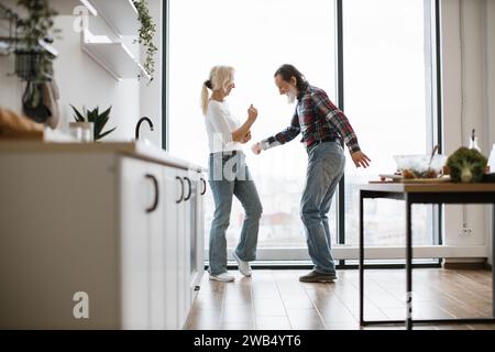 Das alte Paar verbringt Zeit zur freien Verfügung, um in der modernen, hellen Küche einen Twist zu tanzen Stockfoto