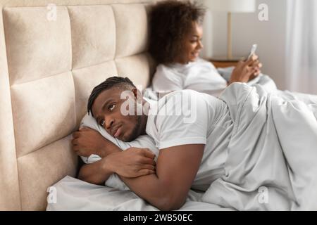 Der schwarze Ehemann war unzufrieden über die Gespräche seiner Frau, die im Bett lag Stockfoto