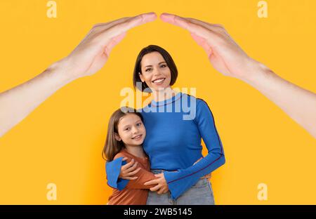 Glückliche Mutter und Tochter, die sich auf gelbem Hintergrund umarmen Stockfoto