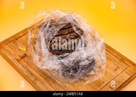 Frisch gebackenes Vollkornbrot in einer Plastiktüte geschnitten, fotografiert auf einem Schneidebrett vor gelbem Hintergrund im Studio Stockfoto