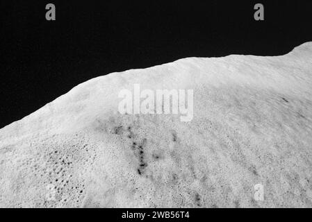 Meist verschwommener schwarzer Sandstrand mit weißem Schaum aus Meereswellen Hintergrund Stockfoto