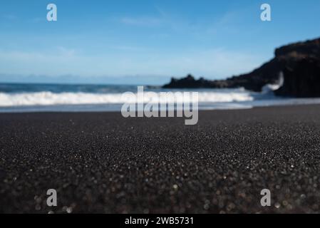 Meist verschwommener schwarzer Sandstrand mit Meereswellen und Himmelshintergrund Stockfoto