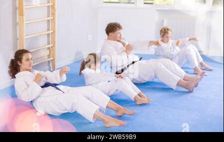 Tweens mit Eltern in Kimonos, die Bauchcrunches mit Schlägen üben Stockfoto