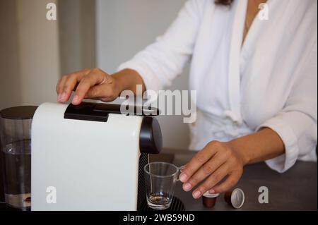 Selektiver Fokus auf eine Kapselkaffeemaschine für den Heimgebrauch und die Frau, die frischen Morgenkaffee zum Frühstück zubereitete, steht an der Küchenzeile. Italienisch Stockfoto