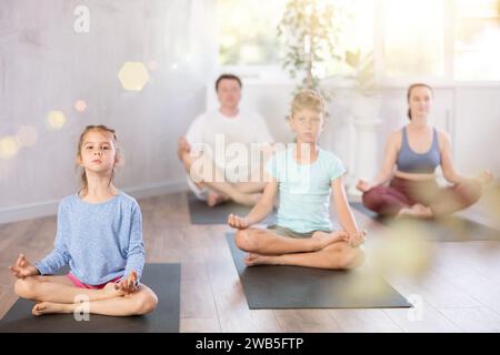 Teenager-Mädchen mit ihren Eltern praktiziert Yoga in Lotusposition Stockfoto