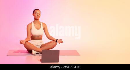 Eine zusammengesetzte Frau mit einem rasierten Kopf sitzt im Kreuz in Lotusposition auf einer Yogamatte Stockfoto