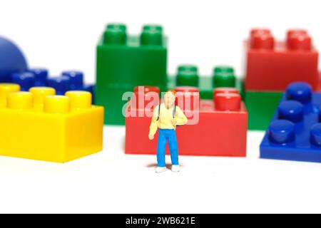 Miniaturmenschen Spielzeug-Fotografie. Ein junger Kindergartenschüler, der vor dem Puzzleblock steht. Isoliert auf weißem Hintergrund. Bild-ph Stockfoto