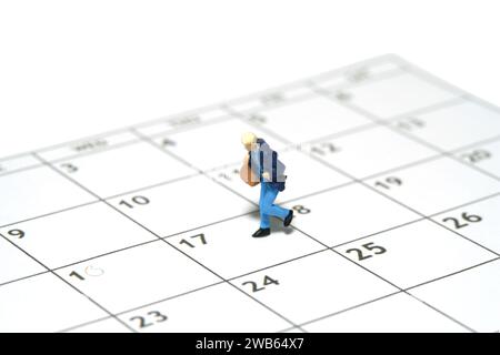 Miniatur-Kleinkinder-Spielfiguren-Fotografie. Eine Studentin, die über den Kalender läuft und eine Reisetasche trägt. Isoliert auf weißem Hintergrund. Bild Stockfoto