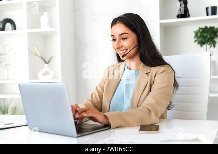Erfolgreiche positive arabische oder indische junge Frau, Call-Center-Operator mit Headset, Arbeit am Support-Helpdesk im Büro mit einem Laptop, lächelnd. Kundendienst Stockfoto