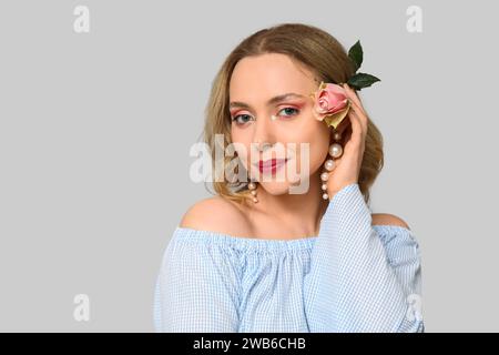 Junge Frau mit schöner Rose auf grauem Hintergrund Stockfoto