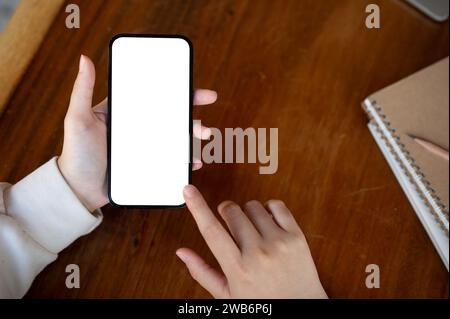 Draufsicht, Eine Frau, die ihr Smartphone am Schreibtisch benutzt. Ein Smartphone-Modell mit weißem Bildschirm. Menschen- und Technologiekonzepte Stockfoto