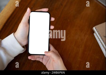 Draufsicht, Eine Frau, die ihr Smartphone am Schreibtisch benutzt. Ein Smartphone-Modell mit weißem Bildschirm. Menschen- und Technologiekonzepte Stockfoto