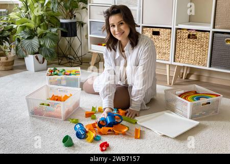 Junge Frau, die kindliches Spielzeug sortiert, Holz Montessori und Kunststoff Details Box Korb von oben Stockfoto