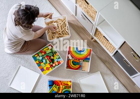 Junge Frau, die kindliches Spielzeug sortiert, Holz Montessori und Kunststoff Details Box Korb von oben Stockfoto