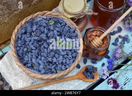 Stillleben mit natürlichem Honig, Wabenschnitt und Geißblatt-Beere mit Blumen auf hölzernem Hintergrund draußen. Ländlicher Sommer ländlicher Backg Stockfoto