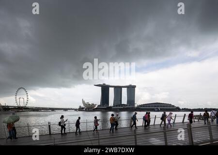 Dunkle Wolken Naturhimmel, düsteres Wetter, Touristen spazieren entlang der Jubiläumsbrücke. Architekturblick auf Marina Bay Sands. Singapur. Stockfoto