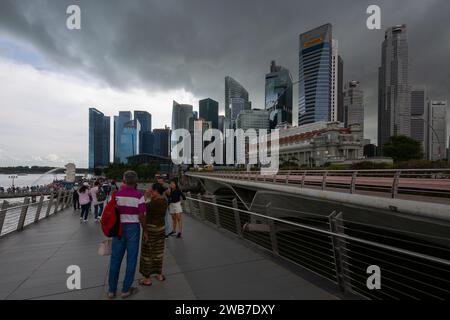 Dunkle Wolken schweben über dem Himmel, als Regen hereinbricht. Touristen im Freien setzen ihre Besichtigungstouren fort, Merlion Park. Singapur. Stockfoto