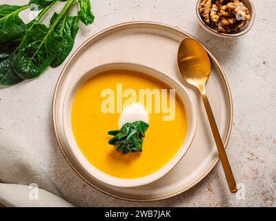 Kürbiscremesuppe serviert Spinat, Nüsse, Sauerrahm. Leckerer hausgemachter Kürbis, süße Kartoffel oder Karottensuppe in der Schüssel auf neutralem Pastelhintergrund. Gemütliche Herbstgerichte. Draufsicht Stockfoto