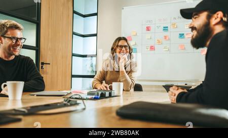 Geschäftsleute, Männer und Frauen, arbeiten in einem modernen Sitzungssaal zusammen. Sie führen ein lebhaftes Gespräch und entwickeln Ideen mit einer vielfältigen Te Stockfoto