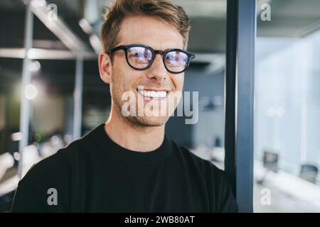 Selbstbewusster männlicher Profi im Büro. Geschäftsmann mit Brille, die in die Kamera lächelt. Techniker, die aktiv am Arbeitsplatz arbeiten. Erfolg Stockfoto
