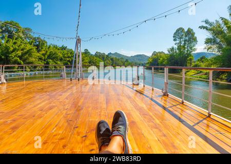 Ein Tourist Fuß, während er sich an Deck entspannt, während er den Fluss Kwai hinunterfährt Stockfoto