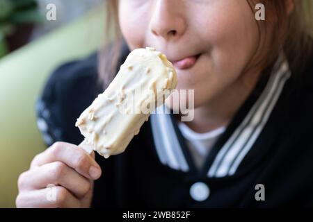 Das kleine asiatische Mädchen öffnet den Mund und isst Eis Stockfoto