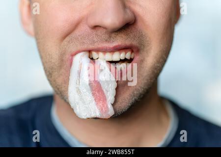 Fetter Speck in einem männlichen Mund in Nahaufnahme. Ein Mann isst ungesunde fetthaltige Nahrung. Stockfoto