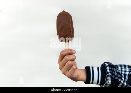 Eis bedeckt mit Schokolade und Mandelstäbchen in der Hand auf weißem Hintergrund. Stockfoto