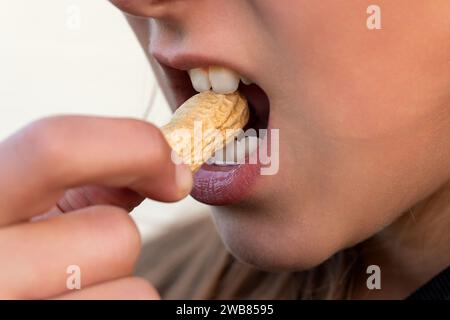 Er isst harte Erdnuss in der Schale. Starke weiße Zähne beißen eine Nuss. Ein offener Mund mit einer harten Nuss. Brechen Sie die Schale der Erdmutter. Stockfoto