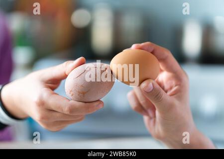 Ostertradition, Eier zu knacken, zwei Hände halten Eier und versuchen, sich gegenseitig das Ei zu brechen, Nahaufnahme vor blauem Hintergrund Stockfoto