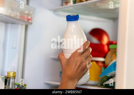 Stellen Sie Milch in den Kühlschrank. Eine Kinderhand nimmt eine Flasche Joghurt aus dem Kühlschrank Stockfoto