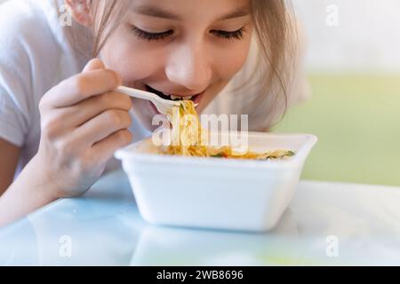 Ein Mädchen isst scharfe koreanische Instant-Nudeln mit Gabeln. Ungesundes Fast Food. Ernährung von Schulkindern Stockfoto