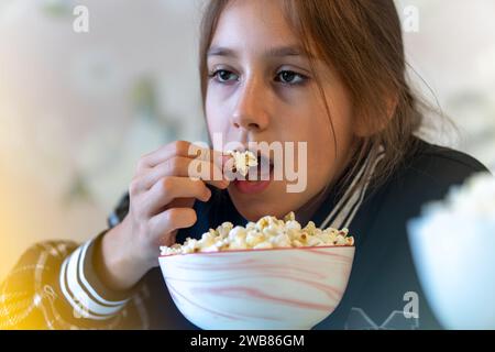 Nahporträt eines netten, attraktiven, fröhlichen, positiven Mädchens, das Popcorn in der Hand hält. Salziges Popcorn im Mund. Junk Food und Kinder. Stockfoto