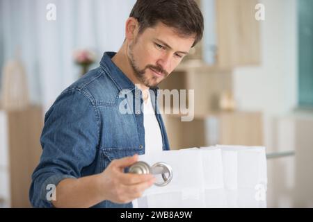 Junger, hübscher Mann, der Fenstervorhang im Zimmer aufgehängt hat Stockfoto