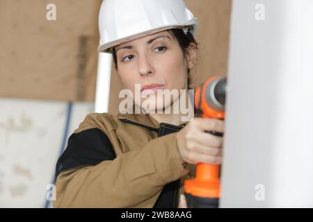 Weibliche Bauherin, die mit Bohrmaschinen an Wänden arbeitet Stockfoto