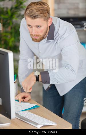 Geschäftsmann, der am Schreibtisch steht und Armbanduhr ansieht Stockfoto