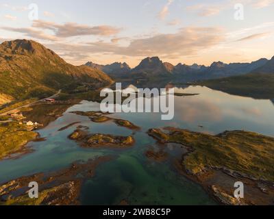 Aus der Vogelperspektive auf einen Fjord in Lofoten, Norwegen mit einem wunderschönen Sonnenuntergang über dem Meer. Ruhiges Wasser, Reflexionen hoher Berge. Stockfoto