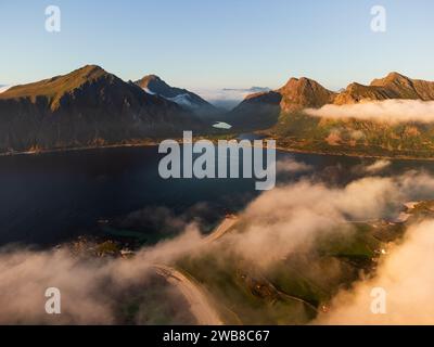 Aus der Vogelperspektive der nördlichen Lofoten bei Sonnenuntergang, blauer Himmel mit flauschigem, niedrigem Nebel. Fjorde und Berge, tiefblaues Meer. Klarer Himmel oben. Stockfoto