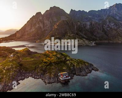 Ein Haus in der Nähe der kleinen Fischerstadt Henningsvaer, Lofoten, Norwegen bei Sonnenuntergang, aus Sicht der Drohne. Klarer blauer Himmel und klare Farben, Berge. Stockfoto