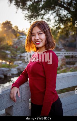 Chinese College Coed Student steht auf der Brücke bei Sonnenuntergang im Huntington's Chinese Garden Stockfoto