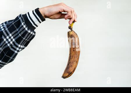 Hässliches Essen. Eine verdorbene Banane in einer Mädchenhand, isoliert auf weißem Hintergrund. Stockfoto