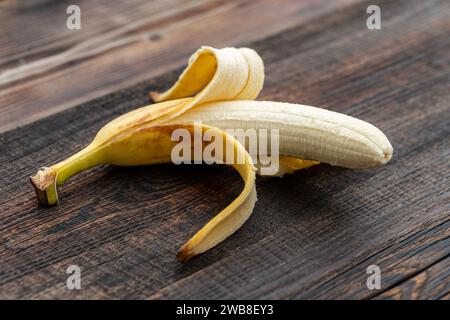 Goldene halbgeschälte Banane, die auf dem Holztisch essen kann. Eine gelbe Banane ohne Schale. Stockfoto