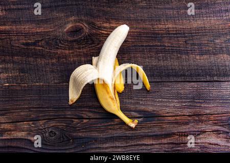 Zusammensetzung von frischen Früchten, ganze frische leckere halbgeschälte Banane ohne Haut auf braunem hölzernem Hintergrund, Ansicht von oben Stockfoto