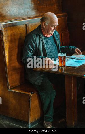 Reifer Mann trinkt Bier und liest Zeitung im Pub, Großbritannien Stockfoto