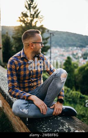 Ein junger Mann im Hemd sitzt lächelnd an einer Burgmauer Stockfoto