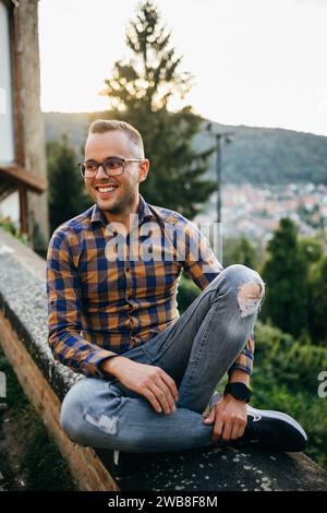 Ein junger Mann im Hemd sitzt lächelnd an einer Burgmauer Stockfoto