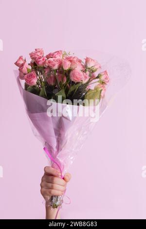 Die Hand eines Kindes hält einen Strauß rosa Rosen auf rosa Hintergrund Stockfoto