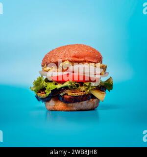 Ein frisch zubereiteter Hamburger auf blauem Hintergrund mit Salat, Tomate, Zwiebeln und Gurken. Stockfoto